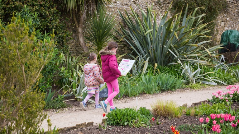 Two young girls walking along path in garden looking at Easter trail packs